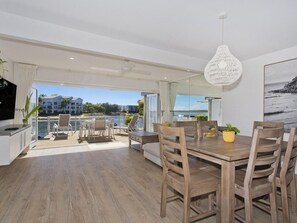 Un balcón amplio con vistas al mar, una zona de comedor con mobiliario de madera y una lámpara colgante moderna.
