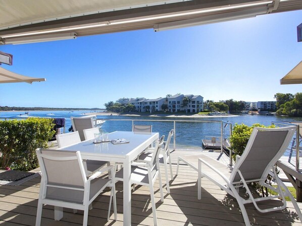 An outdoor deck with a table and chairs, overlooking a body of water and a distant shoreline with buildings.