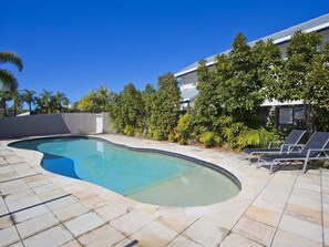 Une piscine à bord incurvé, entourée de chaises longues et bordée d’un bâtiment dont le toit est recouvert de tuiles.