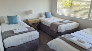 A hotel room with two beds, a bedside table with a lamp, and a window with blinds.