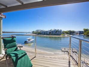 A balcony with a view of a lake, a boat, and a building across the water.