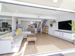 A modern living room with a sofa, coffee table, and TV. There is a staircase leading to an upper level.