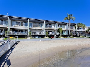 A beachfront hotel with multiple balconies, a sandy beach in the foreground, and palm trees.