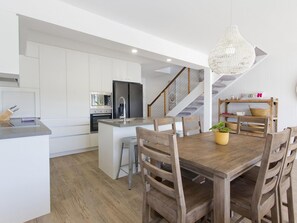 Una cucina moderna con mobili bianchi, un'isola centrale e un'area pranzo con sedie e tavolo in legno.
