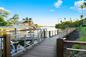 A wooden boardwalk leading to a marina with boats docked, surrounded by greenery and a clear sky. - Jacaranda 12 Hastings Street 12 (Noosa Heads)