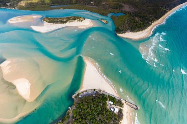 Vista aerea di una zona costiera con acque cristalline, spiagge sabbiose e una piccola isola con edifici.