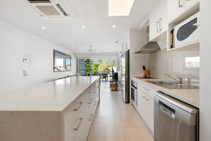 A modern kitchen with a central island, stainless steel appliances, and a view to the outdoors. - Jacaranda 12 Hastings Street 12 (Noosa Heads)