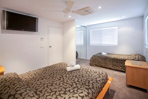 Een hotelkamer met twee bedden, een plafondventilator, een televisie en een raam met jaloezieën.