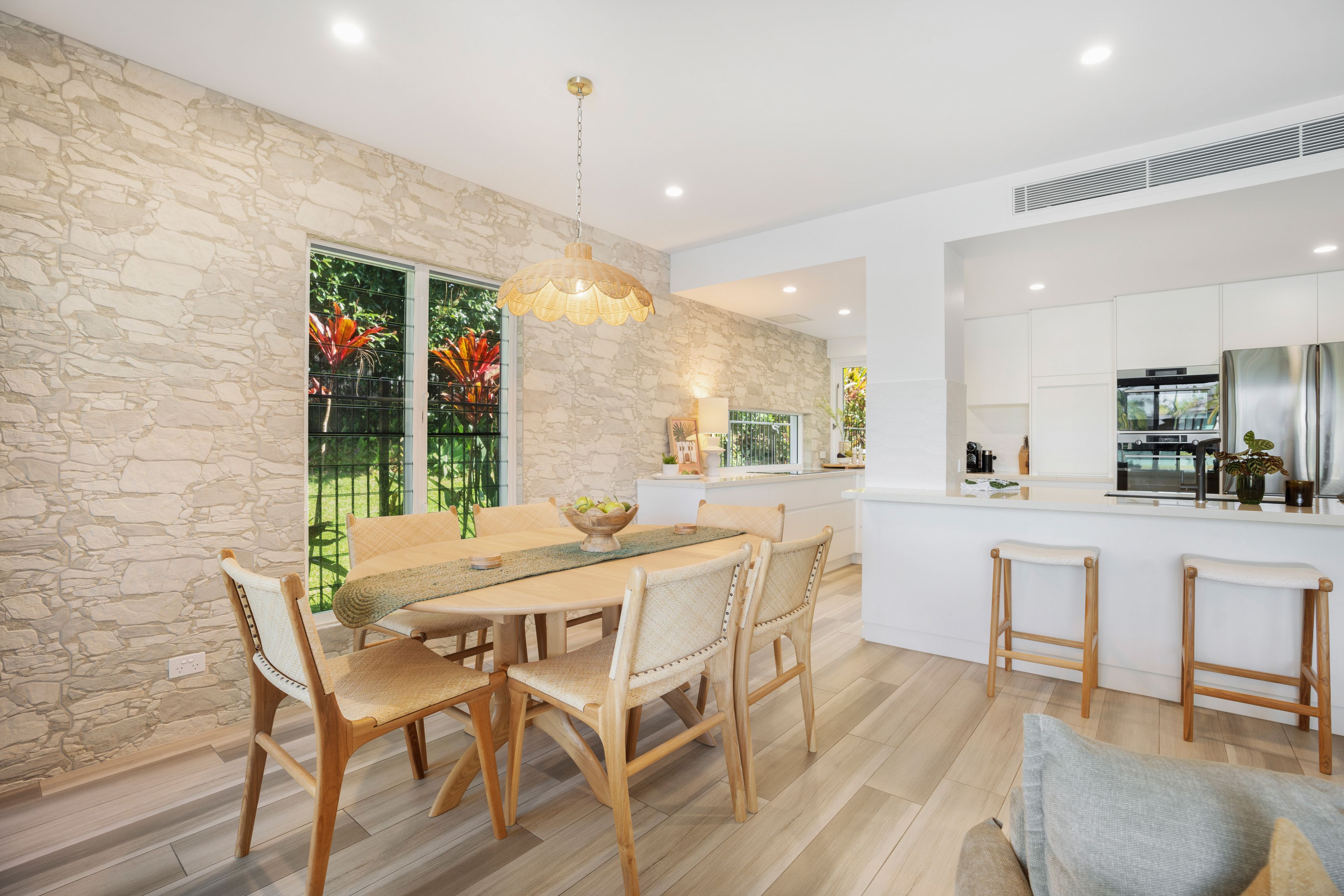 A modern kitchen with a stone accent wall, wooden dining table, and bar stools.