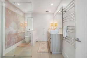 Une salle de bain moderne avec une douche à parois de verre, des toilettes, un lavabo avec un porte-serviettes et un petit tapis.