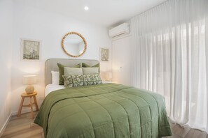 Una camera da letto con un letto, uno specchio tondo, un condizionatore d'aria e una finestra con tende leggere.