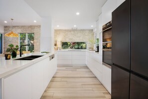Una cocina moderna con armarios blancos, una pared de acento de piedra y una isla grande con lavamanos.
