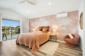Une chambre à coucher comprenant un lit, des tables de chevet, une chaise, une vue sur une piscine et un ventilateur de plafond.