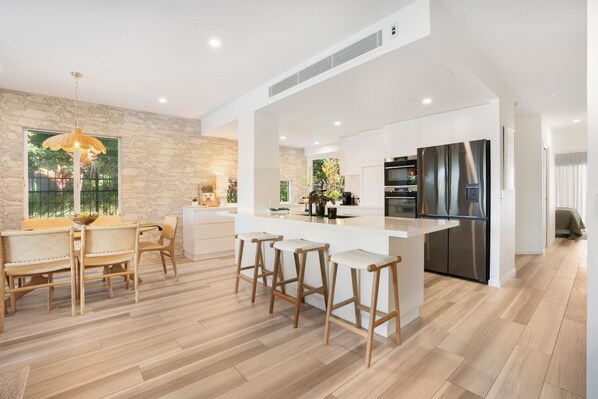 Una cocina moderna con una isla central, taburetes de bar y un comedor con mesa y sillas.