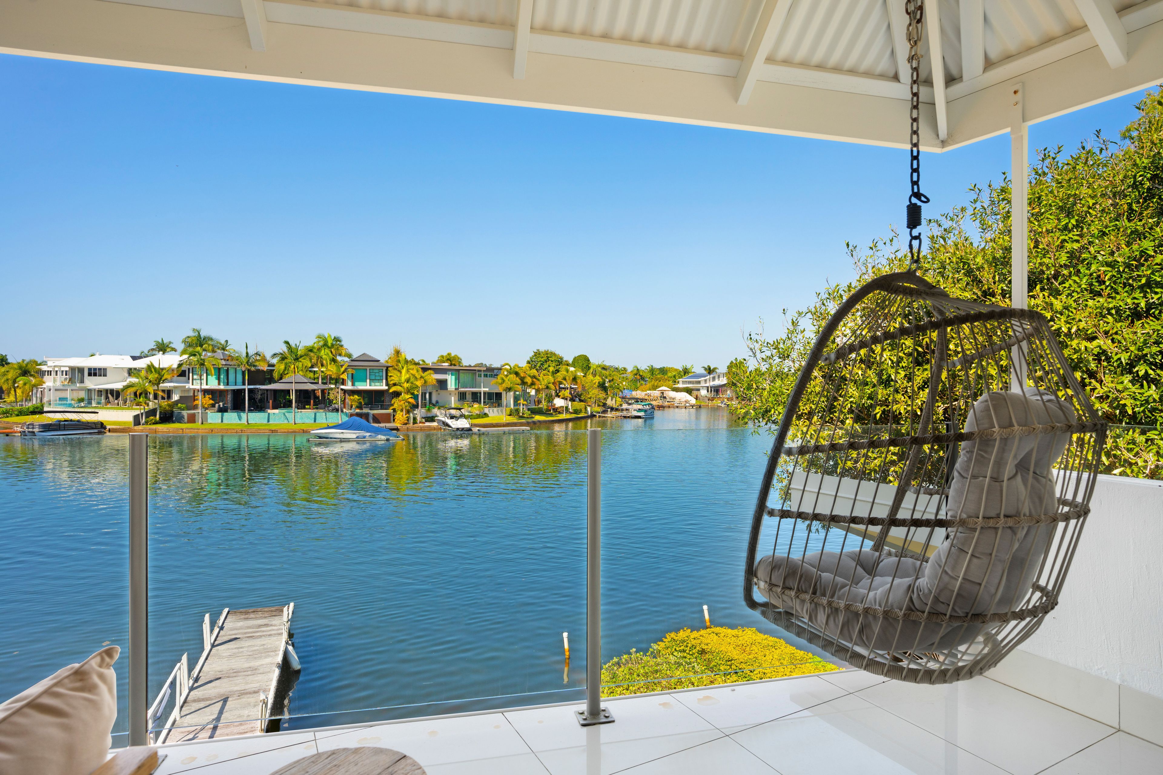 A balcony with a hanging chair overlooking a body of water, a dock, and a row of houses.