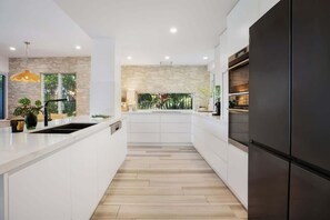 Una cucina moderna con isola centrale, mobili bianchi, una parete a contrasto in pietra e un frigorifero grande.