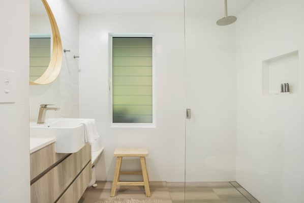 A modern bathroom with a large mirror, a sink, a shower, and a small stool.