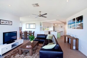 A modern living room with a flat-screen TV, leather sofa, coffee table, and a dining area with chairs and a table.