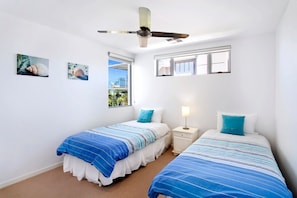 A bedroom with two beds, a ceiling fan, a window, and artwork on the wall.