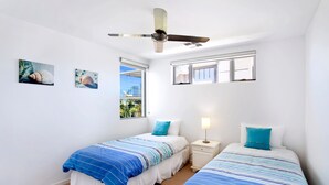 A bedroom with two beds, a ceiling fan, a window with a view, and a nightstand with a lamp.