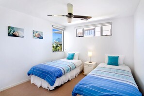 A bedroom with two beds, a ceiling fan, a window with a view, and a nightstand with a lamp. - Alpha On Elanda - Sunshine Beach Haven (Sunshine Beach)