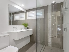 Un bagno moderno con doccia vetrata, lavandino bianco e specchio sopra il mobile.