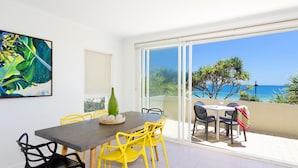 A dining area with a table and chairs, a painting on the wall, and a view of the sea through a glass door.