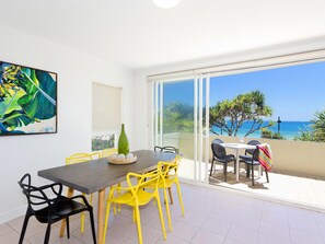 Un comedor con una mesa y sillas, un cuadro en la pared y vista al mar a trav és de un ventanal.