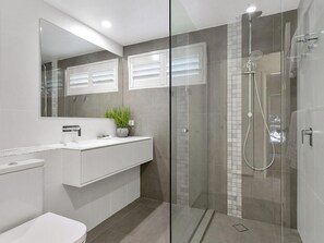 Une salle de bain moderne avec une douche à parois de verre, un lavabo blanc et un miroir au-dessus du meuble-lavabo.