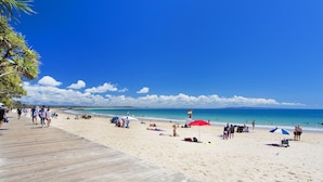 A beach with a wooden boardwalk, people walking, and beach umbrellas.