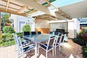 Une terrasse extérieure avec une table et des chaises en verre, un barbecue et un espace abrité agrémenté d’une pergola.