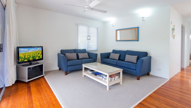 A living room with a flat-screen TV, two sofas, a coffee table, and a ceiling fan. - Dolphins 2 Alderly Terrace 36 (Noosa Heads)