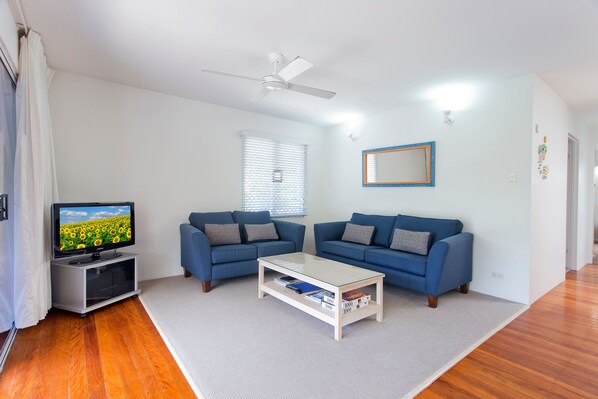 Una sala de estar con una televisión de pantalla plana, dos sofás, una mesa de centro y un ventilador de techo.