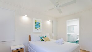 A hotel room with a bed, a nightstand, a framed picture, a ceiling fan, and a bathroom visible through an open door. - Dolphins 2 Alderly Terrace 36 (Noosa Heads)