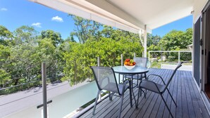 A balcony with a table and chairs, a bowl of fruit, and a view of trees and sky. - Dolphins 2 Alderly Terrace 36 (Noosa Heads)