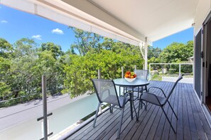 Un balcón con mesa y sillas, un cuenco de fruta y vistas a árboles y cielo.