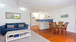 Cozy living space with a kitchenette, sofa, and dining area, featuring a wooden table and wicker chairs.