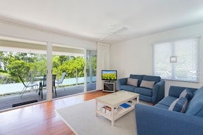 A modern living room with a blue sofa, a coffee table, and a television on a stand. - Dolphins 2 Alderly Terrace 36 (Noosa Heads)
