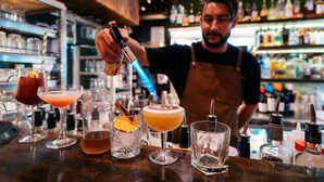 A bartender preparing drinks behind a bar with various bottles and glasses.