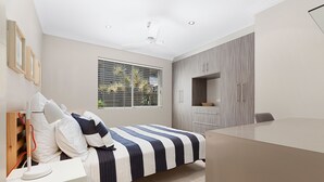 A bedroom with a bed, bedside table, wardrobe, and a window with blinds.
