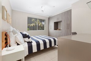 A bedroom with a bed, bedside table, wardrobe, and a window with blinds.