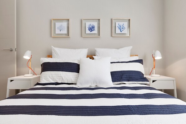 A neatly made bed with a striped bedspread, two bedside lamps, and three framed wall art pieces above it.