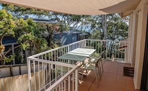 A balcony with a table and chairs, surrounded by a white railing, overlooking a garden and a blue building. - Costa Del Sol 2 Park Road 22 (Noosa Heads)