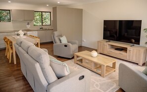 A modern living room with a sofa, armchair, coffee table, and a television on a wooden stand. - Costa Del Sol 2 Park Road 22 (Noosa Heads)