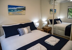 Una camera d'albergo con un letto, un comodino, una lampada, uno specchio e un quadro appeso al muro.