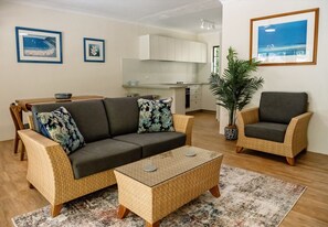 Una sala de estar con sofá, sillón, mesa de centro y un comedor con una cocina al fondo.