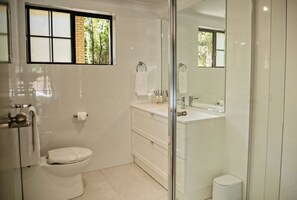 Une salle de bain comprenant des toilettes, un lavabo avec un miroir et une fenêtre donnant sur des arbres.