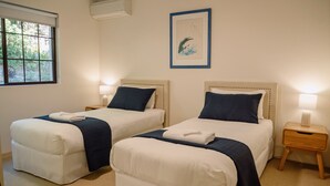 A hotel room with two beds, a window, an air conditioning unit, a framed picture on the wall, and a bedside table with a lamp. - Costa Del Sol 3 Park Road 22 (Noosa Heads)