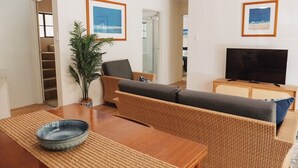 A living room with a sofa, a television, a plant, and a dining table. - Costa Del Sol 3 Park Road 22 (Noosa Heads)