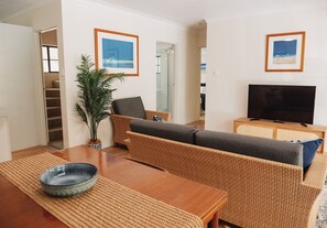 A living room with a sofa, a television, a plant, and a dining table.